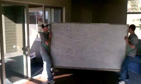 two men carrying a large granite slab through a patio doorway, face visible