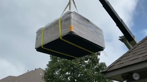 shrink-wrapped hot tub suspended from a delivery crane boom