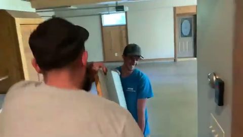 two movers carrying a granite slab through a hallway, face visible