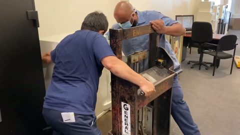two movers gripping a hydraulic safe-jack to move a large black safe