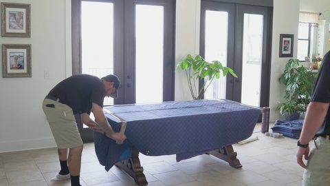 Two movers draping quilted moving blankets over a large wooden dining table