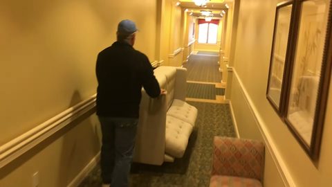 Mover carrying a cream sofa down a hotel style corridor