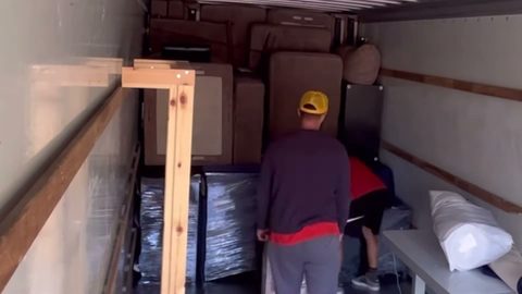 Two-man crew loads padded furniture into the back of a moving truck